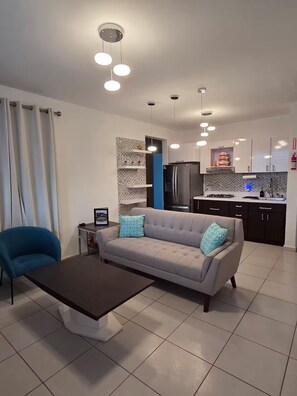 Una sala de estar moderna con un sofá, una mesa de centro y una cocina al fondo.