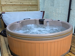 Un bain à remous avec une structure extérieure en bois, un coussin blanc et un tuyau noir.