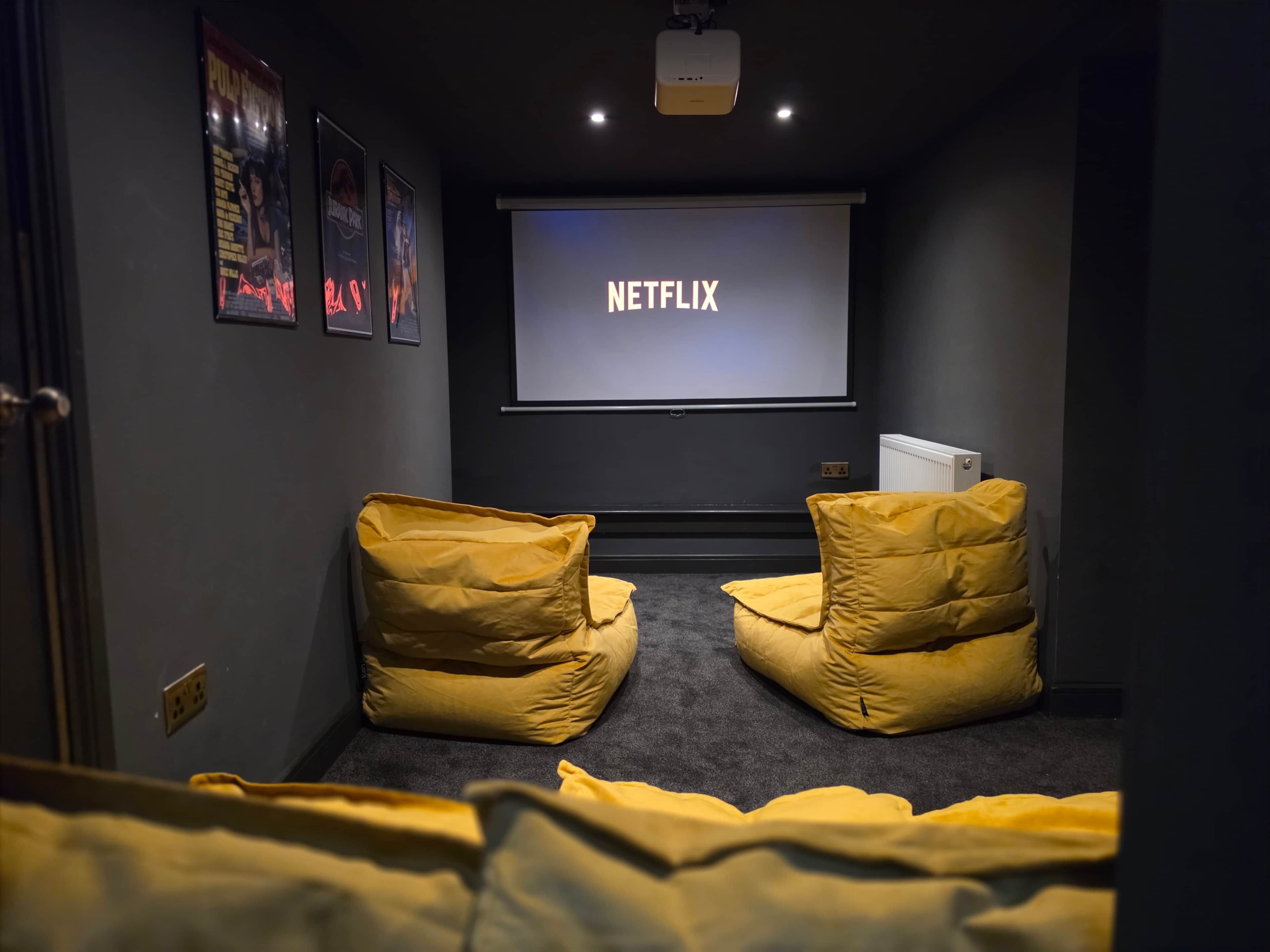 Huoneessa on suuri näyttö, jossa näkyy teksti ”NETFLIX”, sekä kaksi keltaista papupussia.
