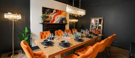 A dining room with a long wooden table set for six, surrounded by orange upholstered chairs.