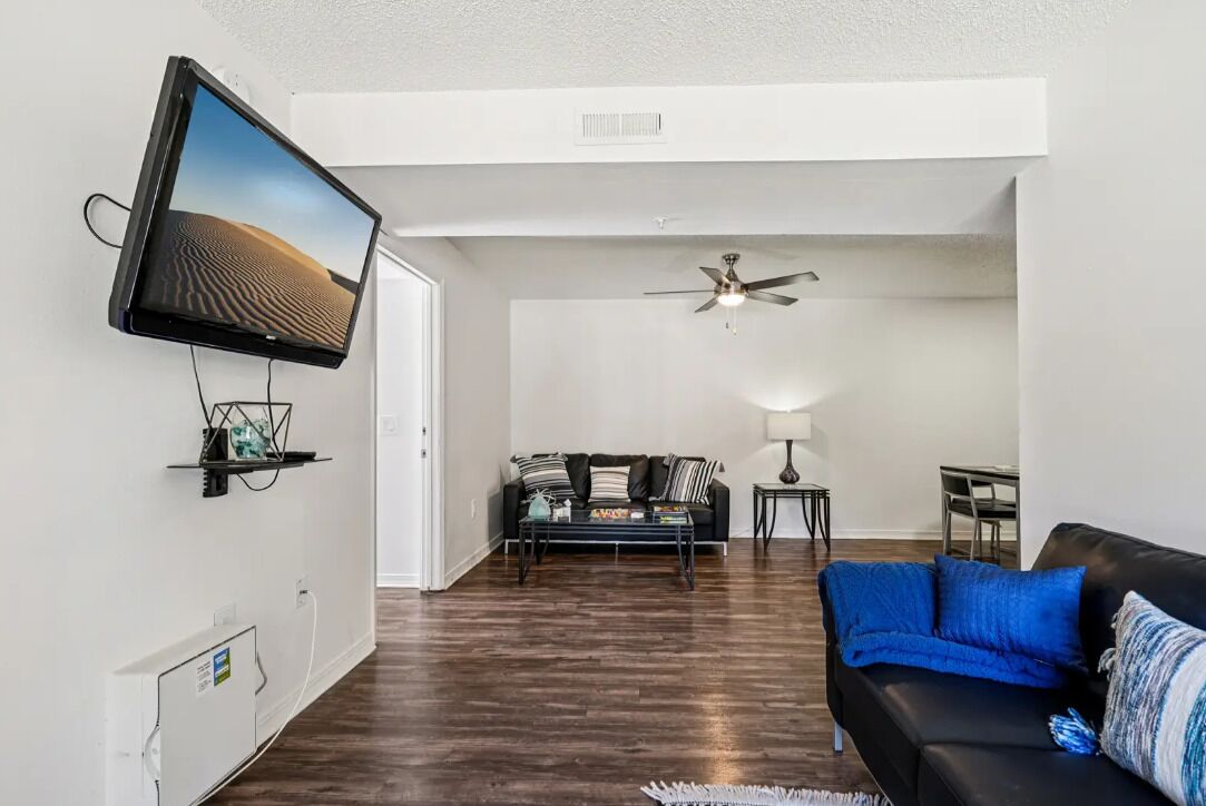 Una sala moderna con un televisor de pantalla plana montado en la pared, un ventilador de techo, un sofá y una mesa de centro.