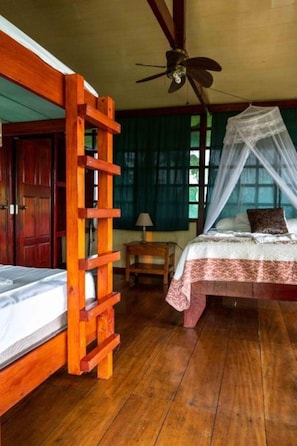 Une chambre avec une échelle en bois, un lit à baldaquin, un ventilateur de plafond et une fenêtre avec des rideaux.