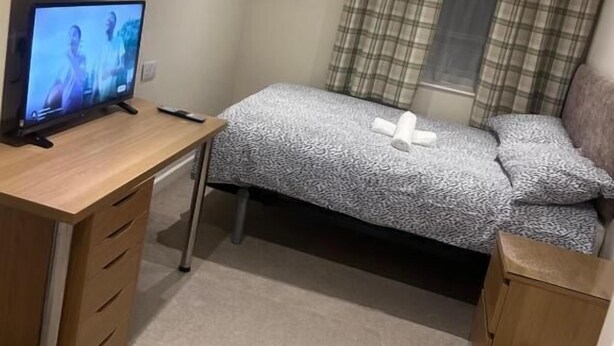 A bedroom with a bed, a desk with a computer, a chair, and a window with curtains.