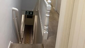 A narrow hallway with a white railing, a fire alarm, and a directional sign.