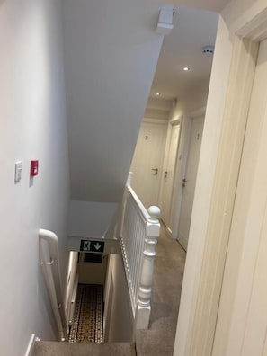 A narrow hallway with a white railing, a fire alarm, and a directional sign.