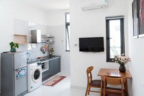 A compact kitchen with a washing machine, a dining area with a table and chairs, and a mounted TV. - Green Apartment near My Khe Beach and Dragon Bridge -R302 (Đà Nẵng)