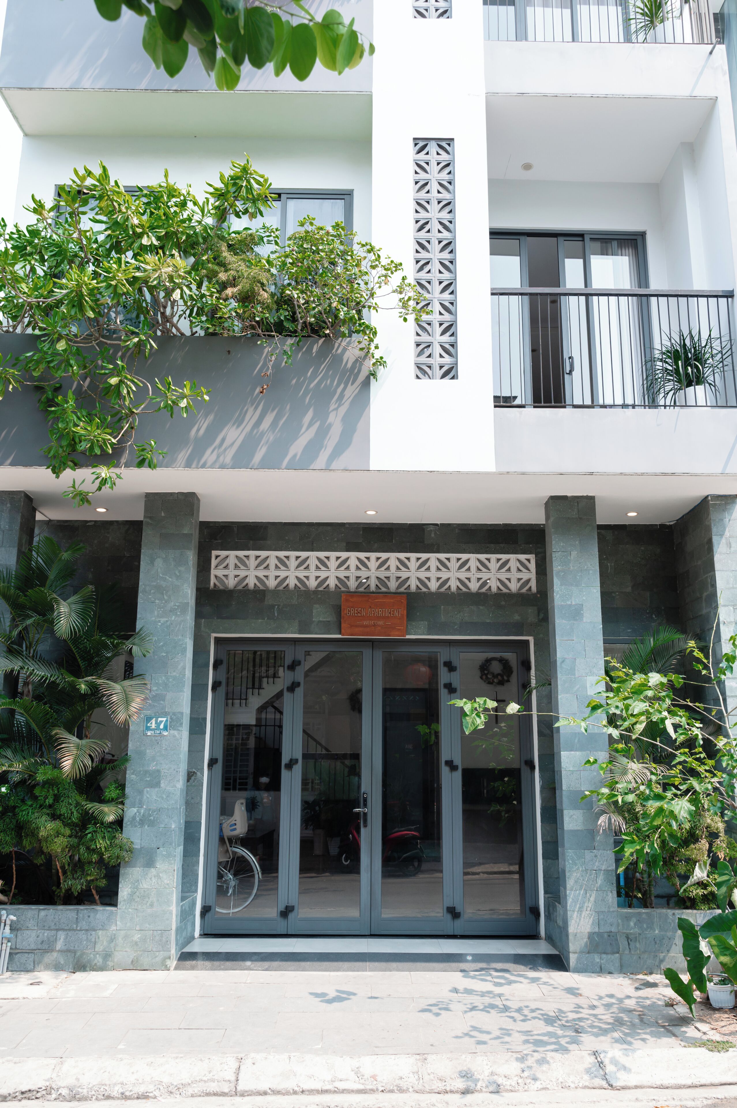 Un immeuble doté d’une entrée moderne, d’une enseigne indiquant « APPARTEMENT ÉCOLOGIQUE » et d’un balcon agrémenté de plantes en pot.