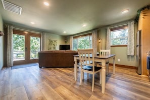 A spacious living area with a wooden floor, a sofa, a dining table with chairs, and a kitchen area with a refrigerator.