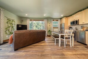 A compact living space with a sofa, dining table, chairs, a TV, and a kitchen area with cabinets and appliances.
