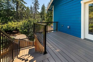 A wooden deck with a black railing, leading to a blue building with a window.