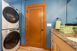 A laundry room with a Whirlpool washer and dryer, a wooden door, and a countertop with folded towels. - Urban Treehouse on Mt. Scott (Portland)