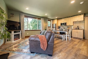 A modern living room with a fireplace, a sofa, and a dining area with a kitchen in the background. - Urban Treehouse on Mt. Scott (Portland)