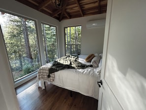 Quarto com cama, janela e vista para uma floresta.