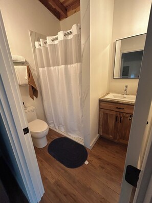 Une salle de bain avec des toilettes blanches, un meuble en bois, un miroir et un rideau de douche.