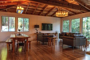 Un vaste espace de vie doté d’un plafond en bois, d’une table à manger avec des chaises, d’un canapé et d’un téléviseur fixé au mur.
