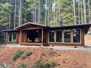 A cabin with a porch, large windows, and a view of a forest.