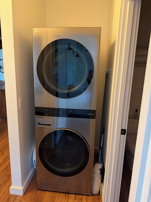 A compact, wall-mounted washer and dryer unit with a circular door design, located in a hallway with wooden flooring.
