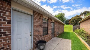 Un immeuble résidentiel doté d’un portail de garage, d’une façade en briques, d’un petit jardin devant avec une pelouse et d’une clôture en bois.