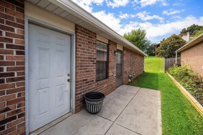 A residential building with a garage door, a brick exterior, a small front yard with a lawn, and a wooden fence.