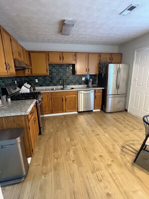 A kitchen with wooden cabinets, a stainless steel refrigerator, a dishwasher, and a granite countertop.