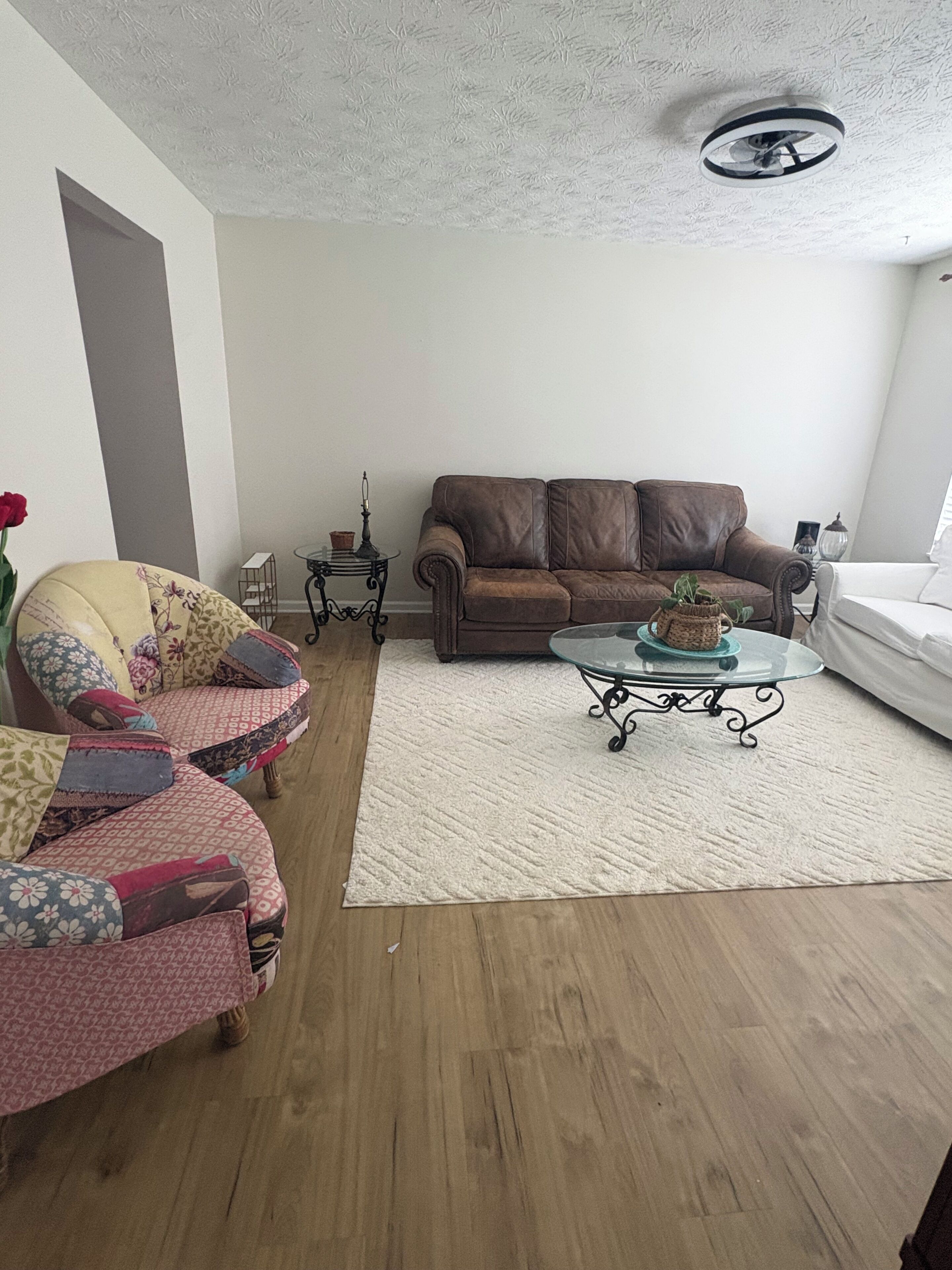Un salon avec un canapé en cuir marron, un fauteuil à motifs, une table basse en verre et un tapis blanc.