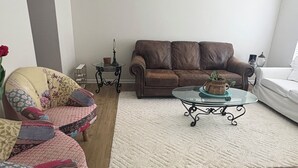 Un salon avec un canapé en cuir marron, un fauteuil à motifs, une table basse en verre et un tapis blanc.