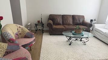 Un salon avec un canapé en cuir marron, un fauteuil à motifs, une table basse en verre et un tapis blanc.
