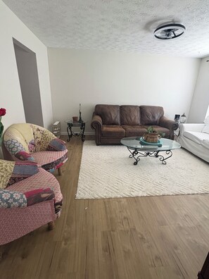A living room with a brown leather sofa, a patterned armchair, a glass coffee table, and a white rug.