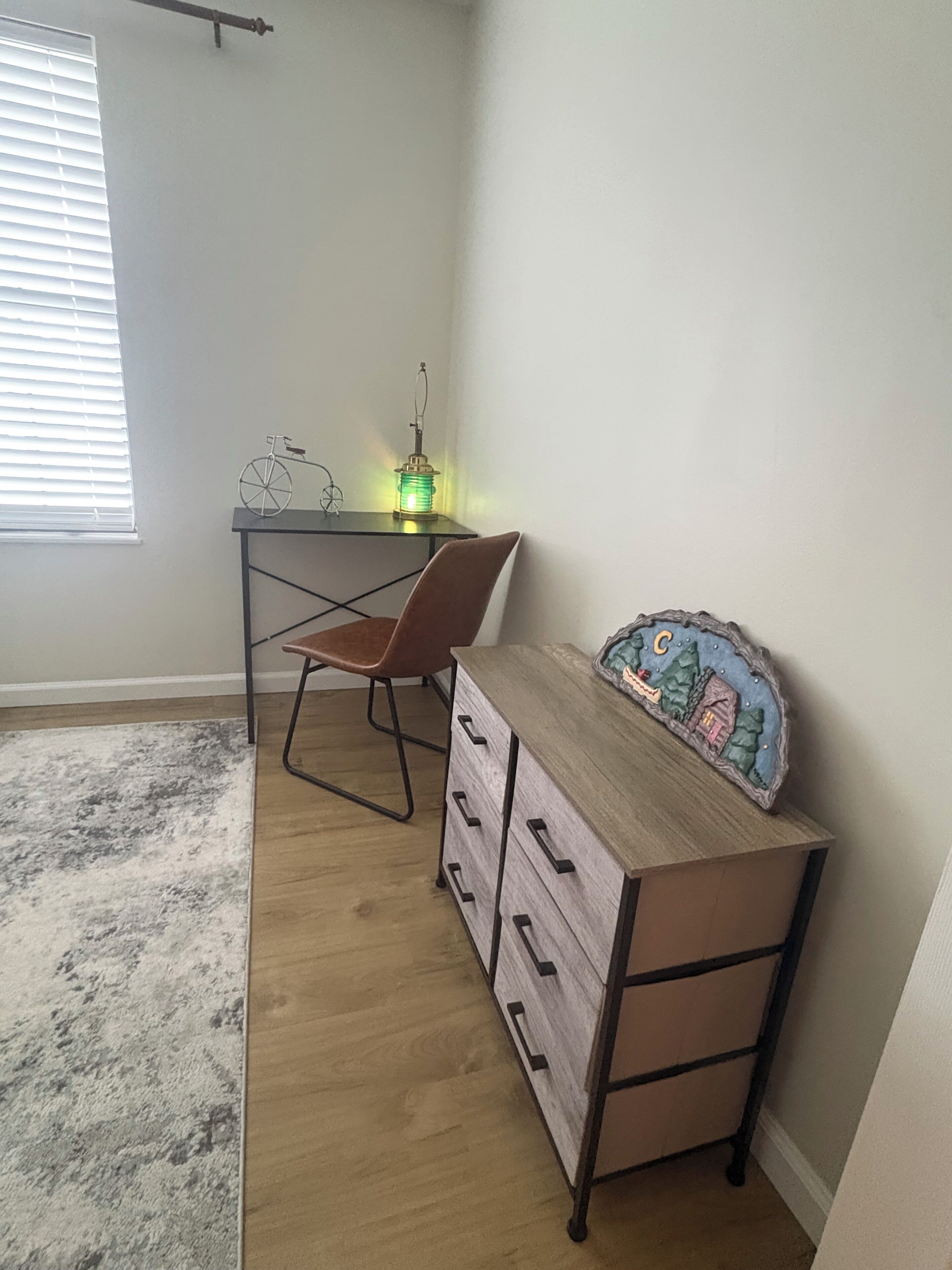 A room with a desk, chair, and a dresser with drawers.