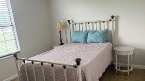 Une chambre à coucher avec un lit à ossature métallique, une table de chevet, une lampe et une fenêtre avec des stores.