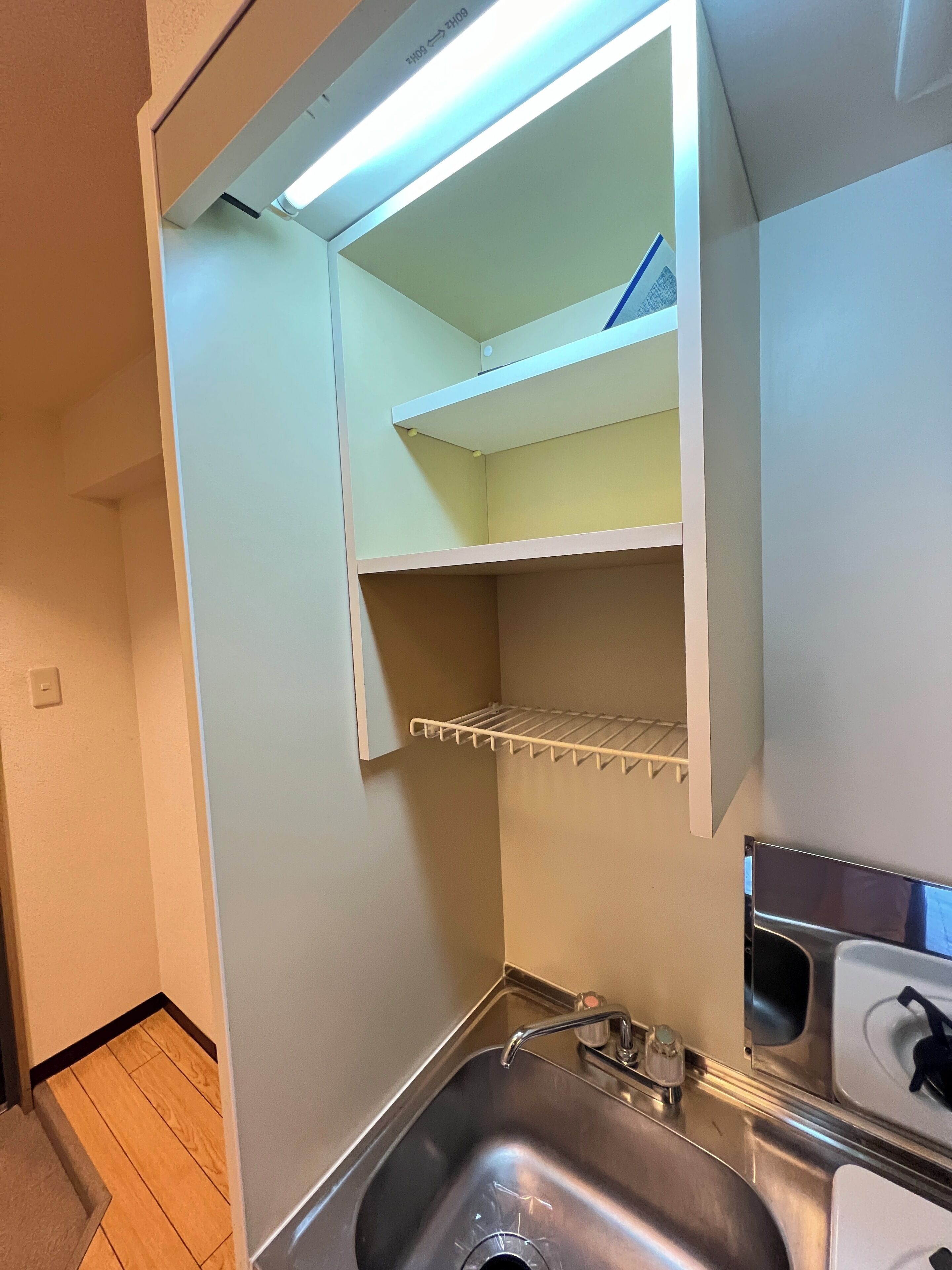 Una cocina con un lavamanos de acero inoxidable, una encimera blanca y un estante empotrado sobre el lavamanos.