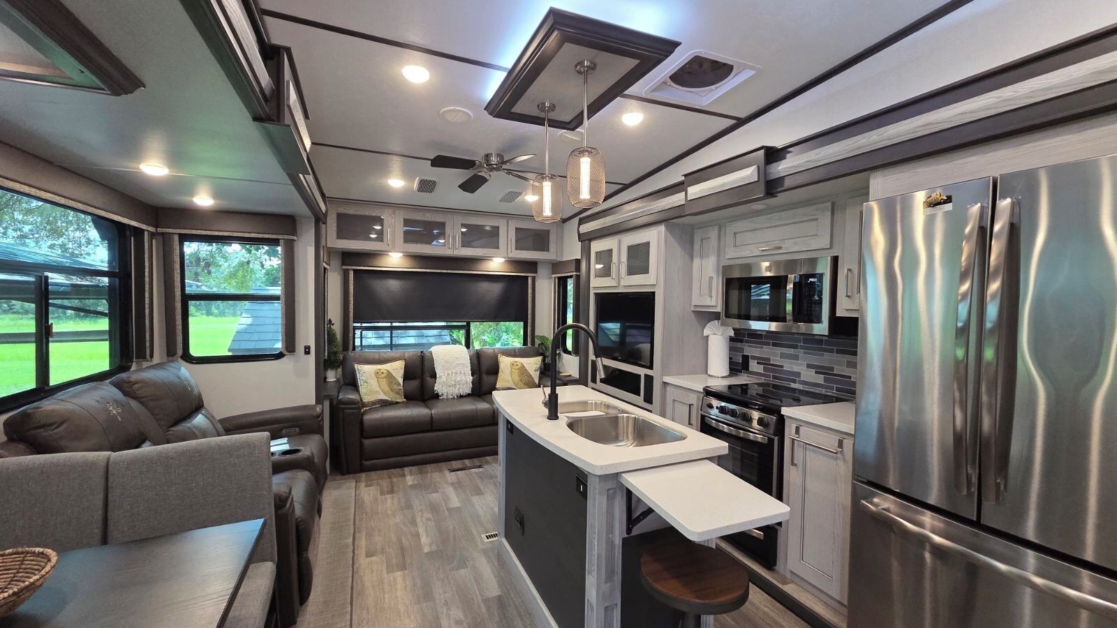 Cocina compacta para autocaravana con una isla central, electrodomésticos de acero inoxidable y un área de descanso con sofá y cojines.