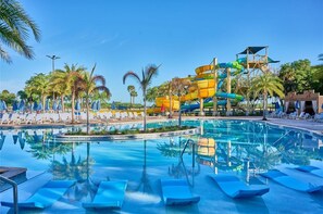 Una piscina con scivoli, lettini e palme.