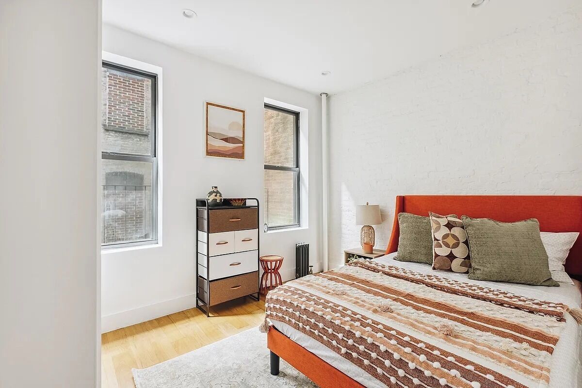 Een slaapkamer met een bed, een dressoir en twee ramen.