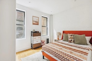 A bedroom with a bed, dresser, and two windows.