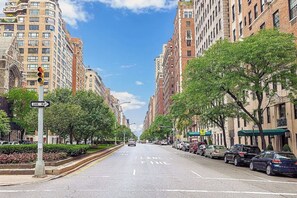 A city street lined with multi-story buildings, a one-way street sign, and parked cars.
