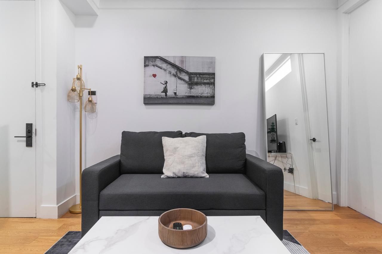 A modern living room with a grey sofa, a white pillow, a wooden coffee table, a floor lamp, and a wall-mounted artwork.