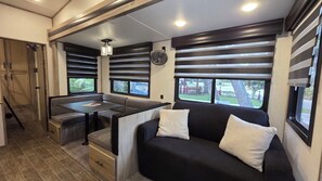 A compact RV interior with a dining area, a sofa, and a fan.