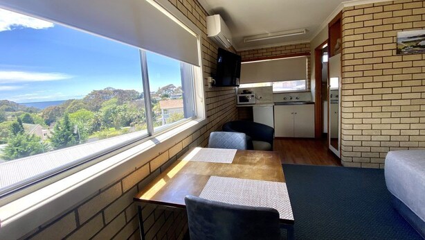 A compact room with a dining table, chairs, a small kitchenette, and a window offering a view of the outdoors.