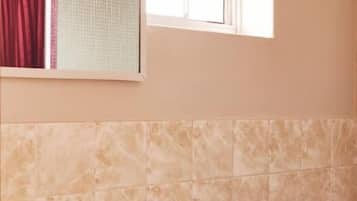 Un baño con lavamanos blanco, un espejo, toallero y dispensador de papel higiénico.