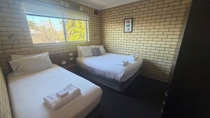 A hotel room with two beds, a window with blinds, a ceiling fan, and a brick wall.