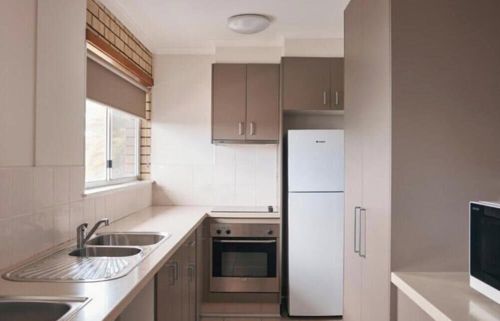 Una cocina compacta con horno empotrado, refrigerador y ventana con persianas.