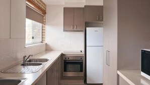 A compact kitchen with a built-in oven, a refrigerator, and a window with blinds.