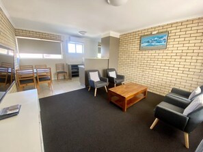A furnished living room with a coffee table, two sofas, and a television mounted on the wall. - Coastal Comfort Motel (Narooma)