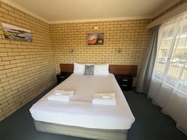 Una habitación de hotel con pared de ladrillo, una cama con ropa blanca, dos mesitas de noche y un cuadro sobre la cabecera.