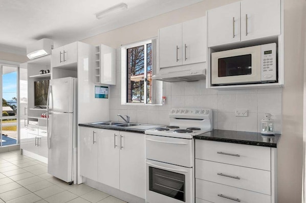 A modern kitchen with white cabinetry, a built-in microwave, a stove, and a refrigerator.