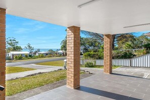 A covered outdoor area with brick pillars, a paved walkway, and a view of a residential street and greenery.