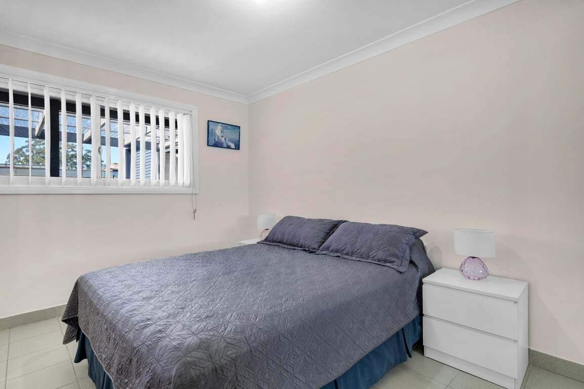 A bedroom with a bed, nightstand, and window.