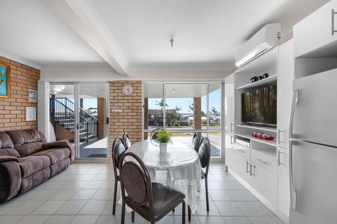 A modern kitchen with a dining area, a sofa, and a view through glass doors.