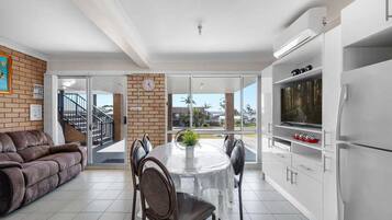 A modern kitchen with a dining area, a sofa, and a view through glass doors.